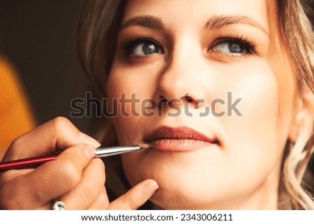 Visagiste make makeup for lovely lady bride at wedding day in hotel room. Close-up of make-up artist with lips brush doing wedding makeup for woman. Concept of luxury wed service. Copy ad text space Royalty-Free Stock Photo #2343006211