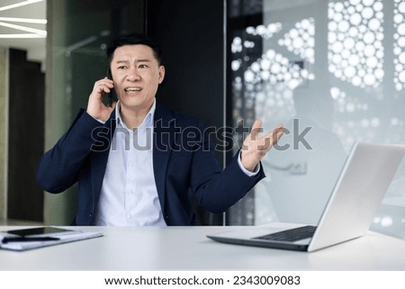 Angry angry asian boss talking on the phone, businessman at workplace shouting into the phone, asian man on interior of office in business suit and investor disappointed. Royalty-Free Stock Photo #2343009083