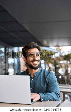 Happy young handsome bearded Latin business man entrepreneur using laptop computer sitting outdoors. Smiling charming Hispanic guy student or professional looking away in city cafe. Royalty-Free Stock Photo #2343014735