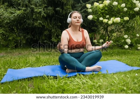 Fat beautiful girl practices yoga in the morning in he garden. Young woman in sportswear outdoors in summer park. Calm black woman, outdoor fitness and breathing in nature 
