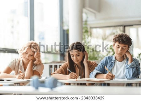 Group of smart pensive school girls and boy studying together, learning language, writing, exam preparation in modern classroom. Back to school, education concept Royalty-Free Stock Photo #2343033429