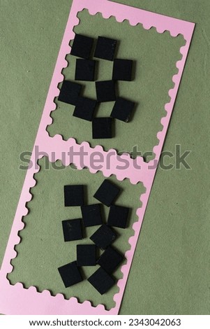 two sets of randomly placed black tiles inside machine-cut pink paper frames on green