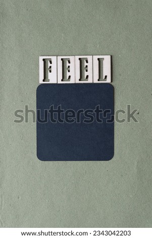 machine-cut rounded corner black paper square and the word "feel" composed of stencil like wooden letters on green