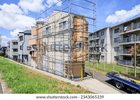 A house with scaffolding for repairing the outer wall and a vehicle for its construction Royalty-Free Stock Photo #2343065339