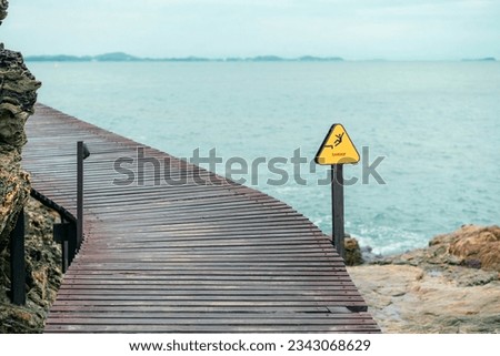 Danger beware falling sign with wooden walkway and sea background 