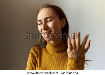 Emotional caucasian young girl standing against gray background with closed eyes and failed facial expression, feeling ashamed and laughing with desperation, gesticulating with regret Royalty-Free Stock Photo #2343084573