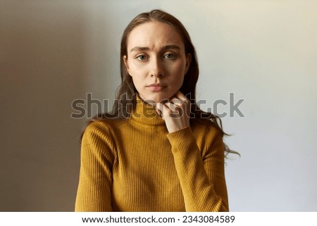 Studio portrait of pretty tired exhausted millennial caucasian female looking at camera with sad face expression, touching her chin, wearing yellow turtleneck. Student girl upset with results of exam Royalty-Free Stock Photo #2343084589