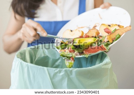 Compost from leftover food asian young housekeeper woman, female hand holding salad bowl use fork scraping waste, rotten vegetable throwing away into garbage, trash or bin. Environmentally responsible Royalty-Free Stock Photo #2343090401