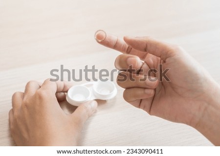 Ophthalmology care, eye sight, vision concept, asian young woman, female hand holding eye lens and putting soft contact lenses on her finger on face from box case on table at home. Healthy eyes care. Royalty-Free Stock Photo #2343090411