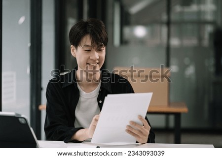 Employee, working with documents sitting at desk using laptop and smartphone at work.