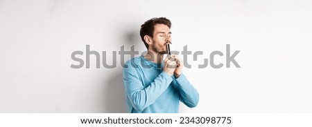 Young man kissing plastic credit card with satisfied face, standing over white background in blue casual shirt. Royalty-Free Stock Photo #2343098775