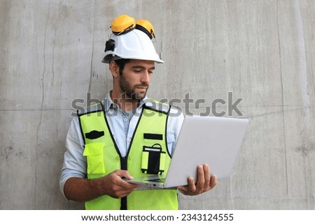 A young attractive bearded supervisor standing outside of the construction site  and checking the plan progress on the laptop.