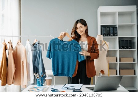 Successful fashion designer. Attractive young asian woman with smile while standing in workshop. Beautiful owner business woman working and holds tablet, laptop and smartphone on desk in studio.