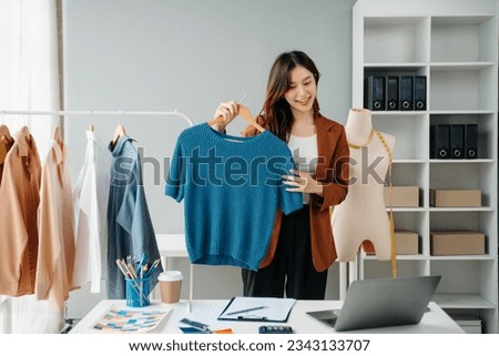 Successful fashion designer. Attractive young asian woman with smile while standing in workshop. Beautiful owner business woman working and holds tablet, laptop and smartphone on desk in studio.