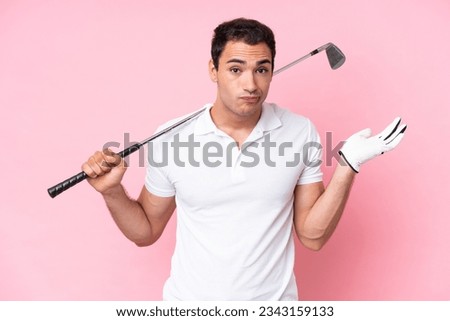 Young golfer player man isolated on pink background having doubts while raising hands