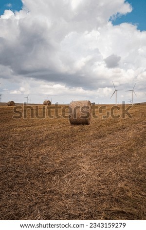 wind farm with freshly harvested wheat field with straw bales. In the distance an ominous stormy sky with black clouds