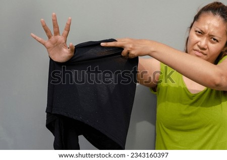 young Asian woman shows her hand to the hole of her old black pants, torn buttocks after being used for a long time. grey background