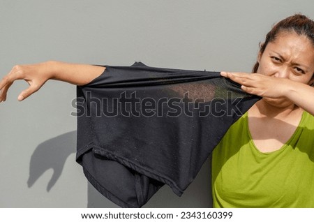 young Asian woman shows her arm to the hole of her old black pants, torn buttocks after being used for a long time. grey background