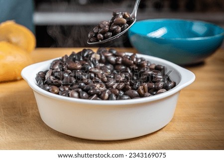 Cooked black beans in a white bowl on a wooden table being mixed Royalty-Free Stock Photo #2343169075
