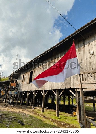 in order to celebrate indonesian independence August 17th, raising the flag in an open space, next to an ancient wooden house in the village