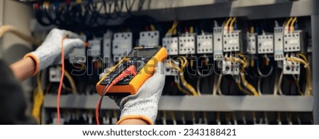 Electrician engineer uses a multimeter to test the electrical installation and power line current in an electrical system control cabinet. Royalty-Free Stock Photo #2343188421