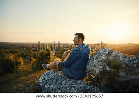 Adult man enjoying sunset sitting on top of the mountain  Royalty-Free Stock Photo #2343195657