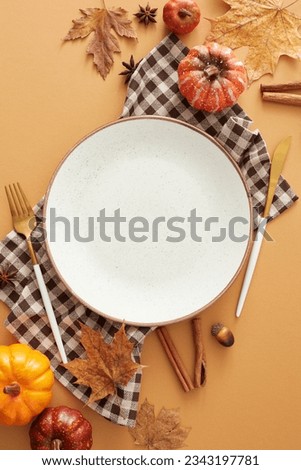 Seasonal decor inspiration idea. Top view shot of blank plate, cutlery, checkered napkin, autumnal decorations on pastel brown background