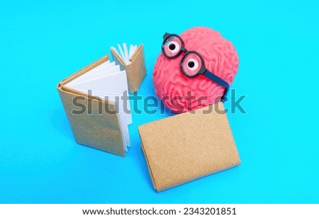 Close-up of a cute character made from a human brain model and googly eyes with glasses reads books isolated on blue background. Joy of education and discovery.