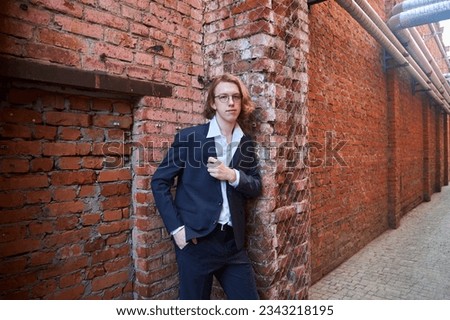 A handsome young man in a pantsuit. European. A college or university student. Street photo shoot near a brick wall