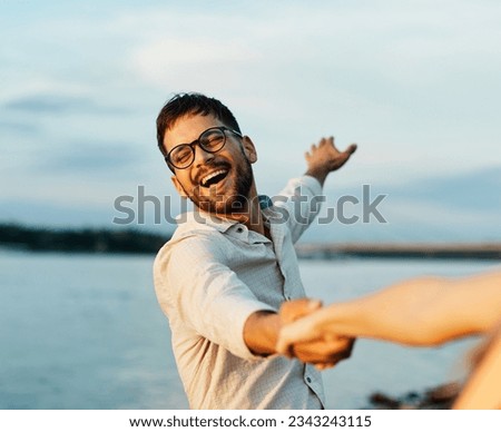 Portrait of a young happy man and couple having fun outdoors in nature during sunset. Girlfriend and boyfriend bonding, love concept during summer, holding hands and dancing and swinging