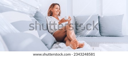 Beautiful barefoot woman dressed white shirt relaxing on luxury terrace with espresso cup patio on the comfortable sofa pillows and enjoying midday time. Carefree life or coffee break concept image
