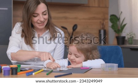 A young mother teaches her daughter to draw. They have fun at home. A happy family.