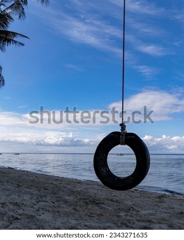 Close-up of a tire swing hanging from a palm tree on the beach in Siquijor, an island in the Philippines, with the silhouette of a fisherman in the tire.