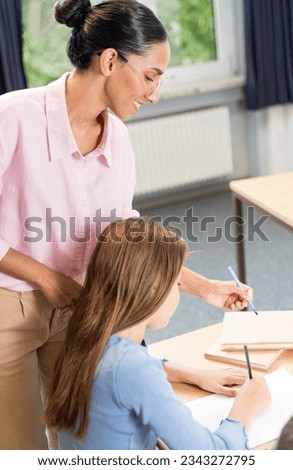 Smiling female lecturer helping student during her class. Student with helpful teacher. Vertical photo of female teacher and schoolgirl in the classroom. Assistance in learning prompting and mentoring