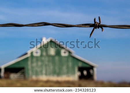 The barbed wire fence with old rural barn in the background.