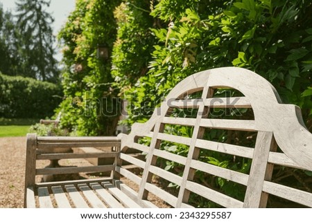 Shallow focus of a a wooden bench seen on the driveway, next to a large country house. Wisteria can be seen growing on the facade.