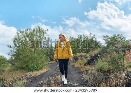 Happy young woman hiker walking on black sand lava-rocky terrain of Mount Etna, enjoying freedom and admiring panoramic view.