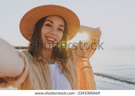 Close up smiling young woman 20s in straw hat shirt summer casual clothes do selfie shot mobile cell phone outdoors at sunrise sun dawn over sea background People vacation lifestyle journey concept.