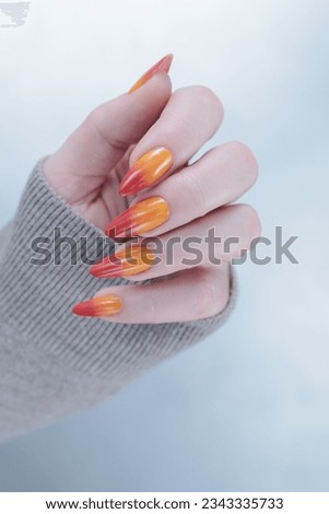 Female beautiful hand with long nails and a bright yellow orange and red nail polish