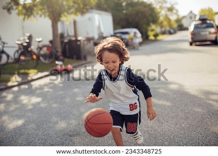 Young boy playing with a basketball on the street in the suburbs Royalty-Free Stock Photo #2343348725