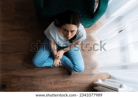 View from above at depressed Caucasian young woman sitting crossed legs on floor. Concept of depression, psychology and mental health problems. Royalty-Free Stock Photo #2343377989