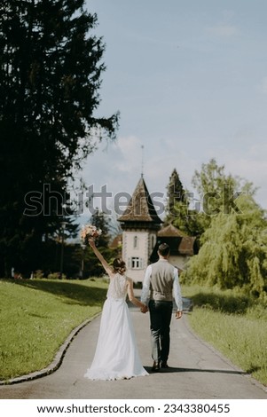 Beautiful bride and groom standing on the village street with castle background. A bride lifting her arms to show the flower bouquet