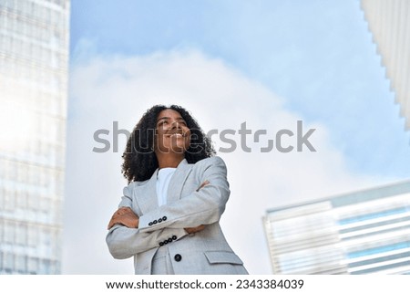 Happy smiling confident young African American professional business woman leader wearing suit standing in big city on street arms crossed thinking of success, dreaming, feeling proud outdoors.