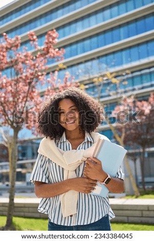 Happy smiling African American girl student standing outside university looking at camera outdoors, vertical portrait. Applying foreign university, study abroad, admission and scholarship program. Royalty-Free Stock Photo #2343384045