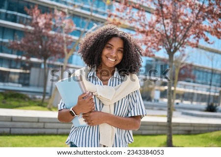 Happy pretty female African American girl student standing outside university holding notebooks looking at camera outdoors, portrait. Applying university, admission and scholarship program concept. Royalty-Free Stock Photo #2343384053