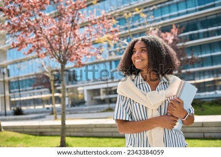 Happy smiling African American girl student standing in university park looking away outdoor dreaming of applying foreign university, study abroad, thinking of admission and scholarship, copy space. Royalty-Free Stock Photo #2343384059