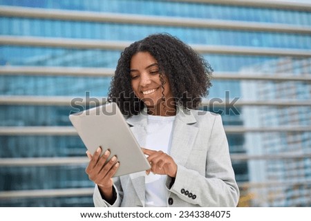 Happy young African American business woman holding digital tablet standing in city street, smiling busy sales professional ethnic lady corporate leader executive working outside office.