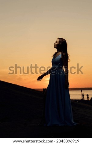 A girl in a dress against the background of the river and the setting sun