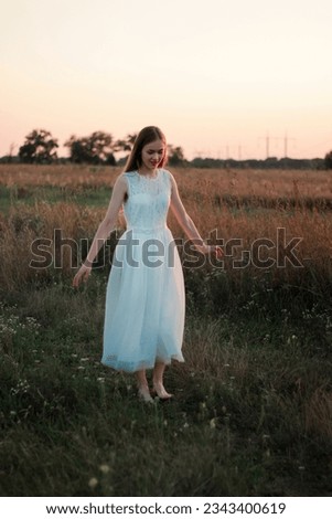 A beautiful pretty girl is dancing on a field at sunset in a white dress. Happy woman. Concept. Bride