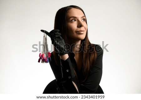 Elegant darkhair woman nails master wearing black uniform showing palette with nail polish colors samples, white background. Beauty industry Royalty-Free Stock Photo #2343401959